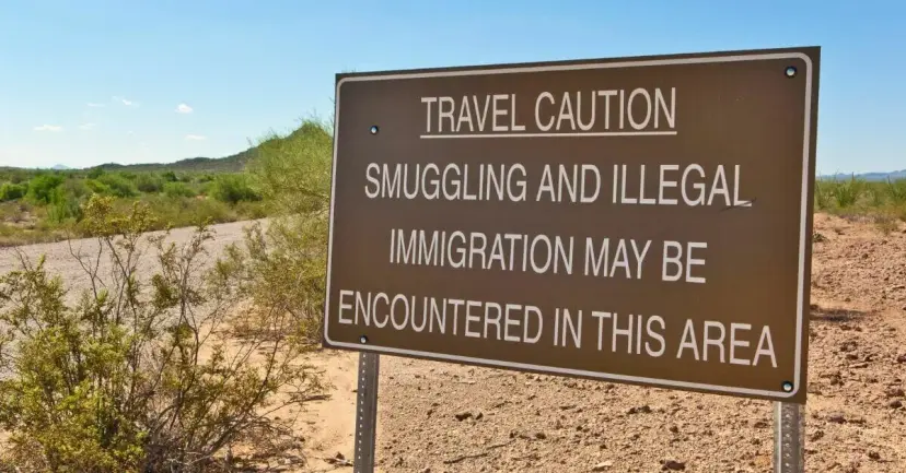 Roadside sign in the desert reading 'Travel caution: smuggling and illegal immigration may be encountered in this area.'