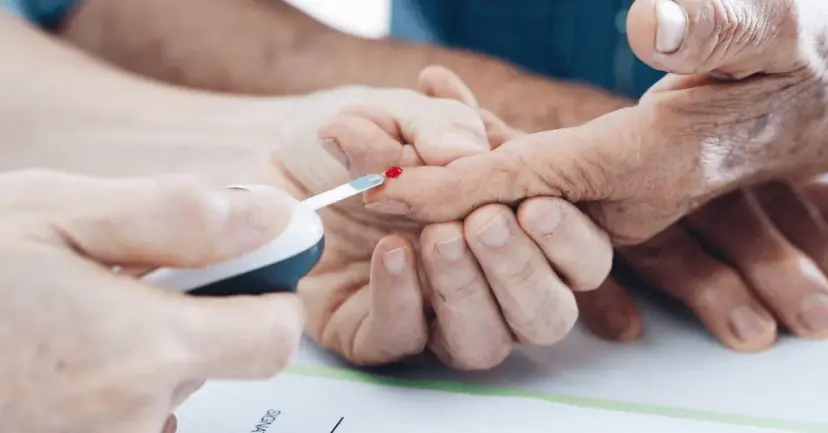 Close-up of hands pricking a senior's fingertip with a glucose meter test strip.