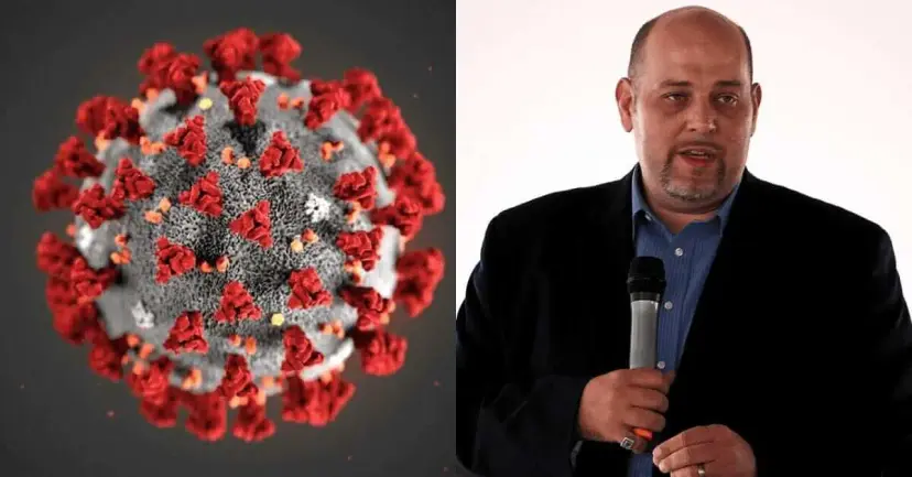 A coronavirus illustration beside a man in a dark jacket speaking into a microphone.