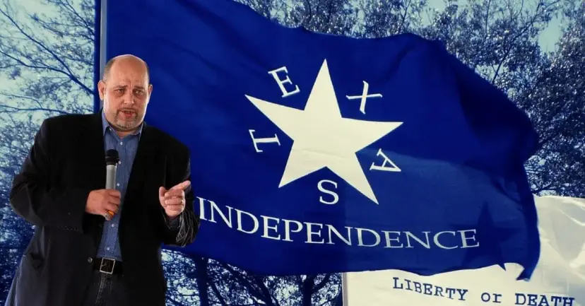 Daniel Miller speaks into a microphone in front of a blue Texas Independence flag reading 'Liberty or Death.'