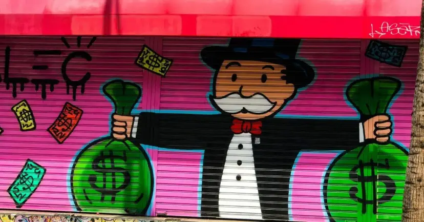 Graffiti mural of the Monopoly man holding bags of money on a pink storefront shutter.