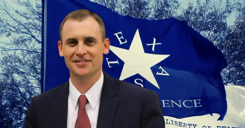 State Representative Andrew Murr smiling in front of a blue flag reading 'Texas Independence.'