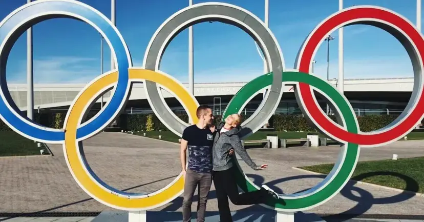 Two young men pose inside a large sculpture of the Olympic rings.