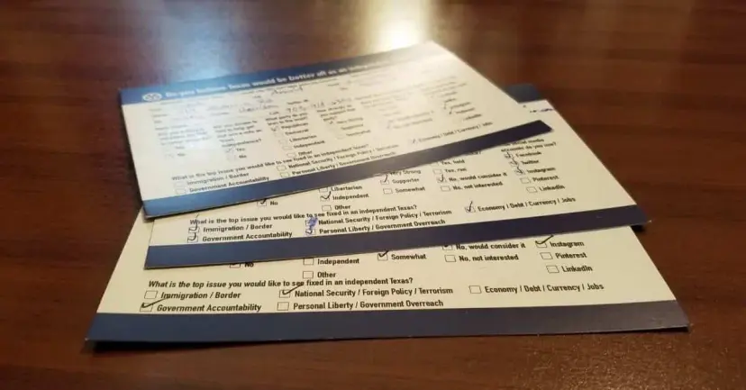 Two filled-out survey cards asking about an independent Texas, lying on a wooden table.