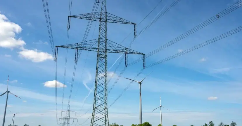 High-voltage power line towers and wind turbines under a blue sky.