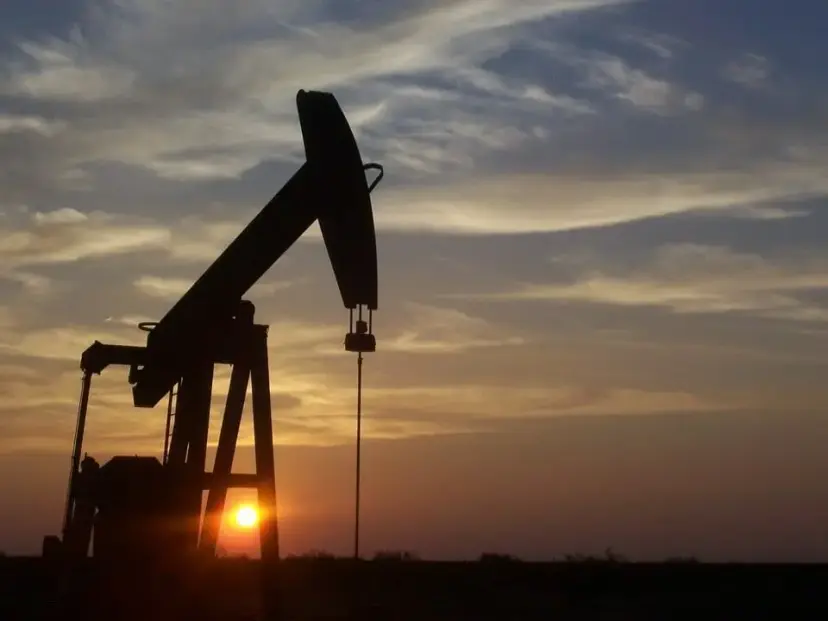 Silhouette of an oil pumpjack against a cloudy sunset sky.