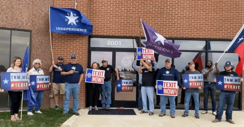 Supporters holding Texas Independence flags and 'TEXIT Now' signs stand outside a brick building.