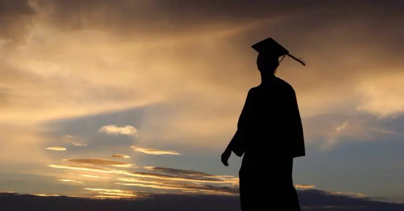 Silhouette of a graduate in cap and gown against a golden sunset sky.