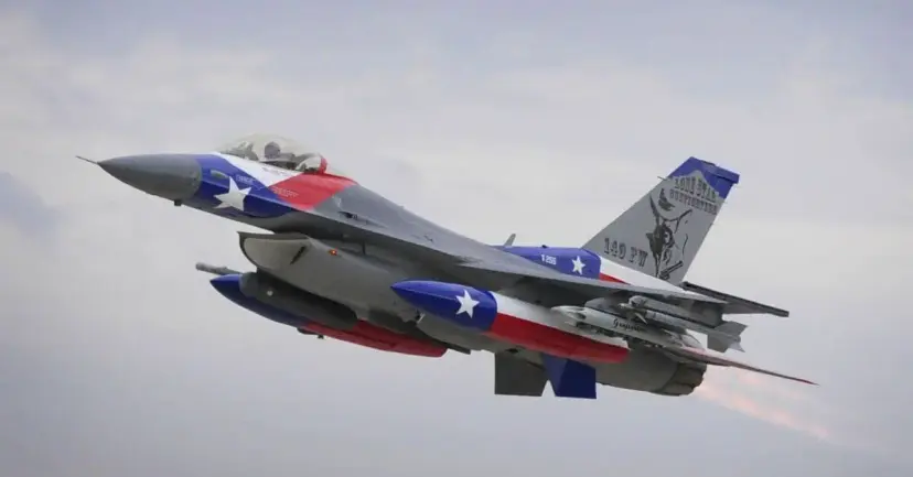An F-16 fighter jet painted in Texas flag colors in flight against a cloudy sky.