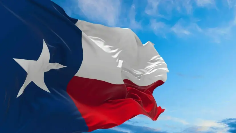 Texas flag waving against a bright blue sky with scattered clouds.