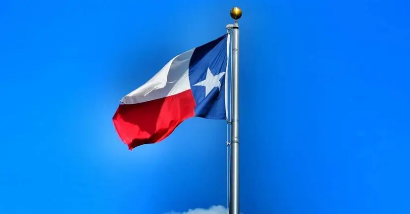 Texas flag flying from a flagpole against a bright blue sky.