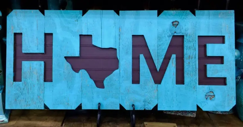 A wooden sign spelling 'Home' with the letter O cut out in the shape of Texas.