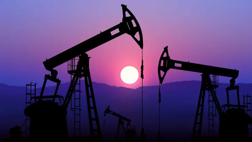 Silhouettes of oil pump jacks against a purple and pink sunset sky