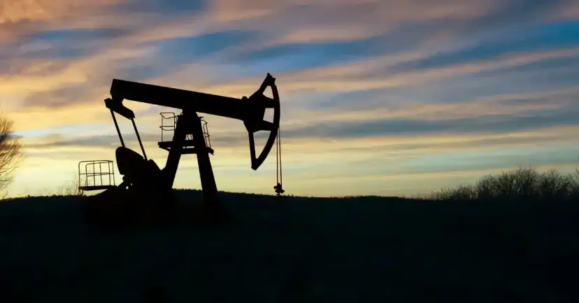 Silhouette of an oil pumpjack in a field against a sunset sky.