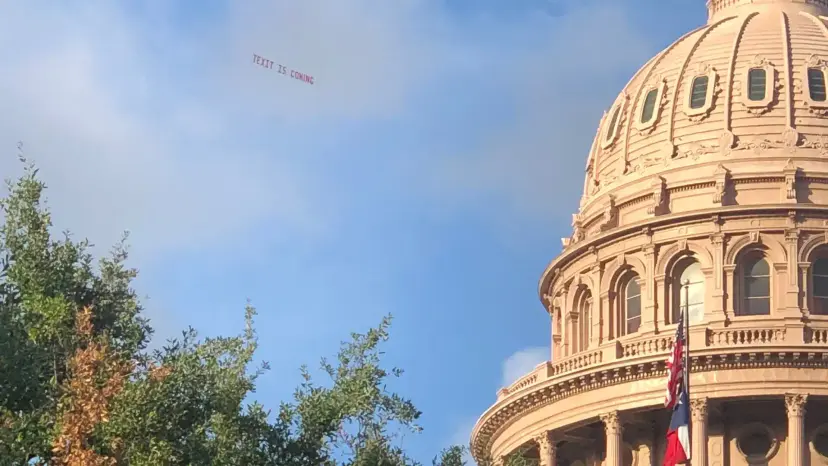 Texas Capitol dome with a plane towing a TEXIT banner in the sky above the trees