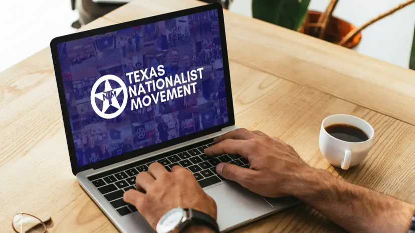 Hands typing on a laptop showing the Texas Nationalist Movement logo, with a cup of coffee nearby.