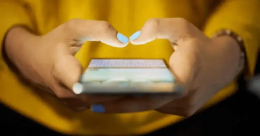 Close view of a person in a yellow top holding a smartphone in both hands.