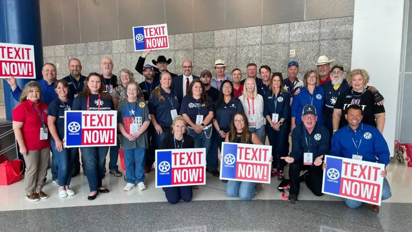 Large group of TNM volunteers in matching shirts holding TEXIT NOW signs in a convention hall
