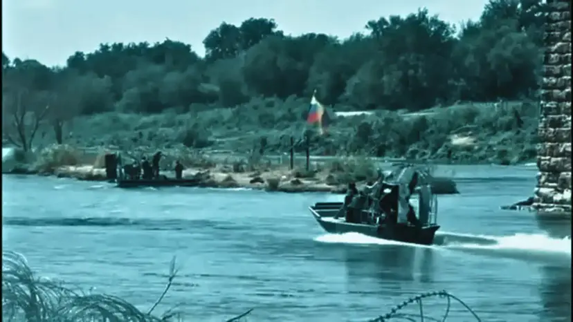 Airboats patrol the Rio Grande near a riverbank where a small flag stands among brush.