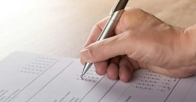 A hand holding a pen marks a box on a paper ballot.
