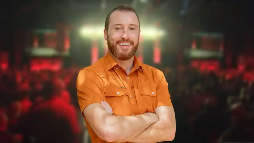 Jonathan LaBar smiling with arms crossed in an orange shirt in front of a blurred event crowd.