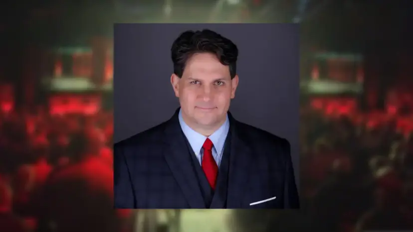 Portrait of Stephen Kallas in a dark suit and red tie over a blurred event background.