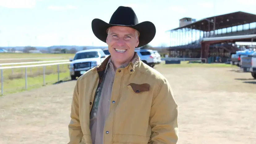 Kyle Biedermann in a black cowboy hat and tan jacket smiles at an outdoor fairground.