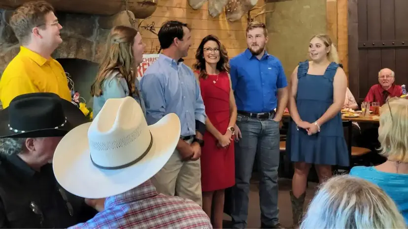 A woman in a red dress stands with a group of young adults as guests watch a campaign kickoff.