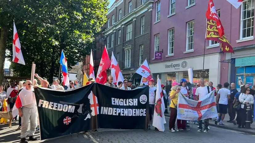 Marchers carry St. George's Cross flags and banners reading 'Freedom' and 'English Independence' down a city street.