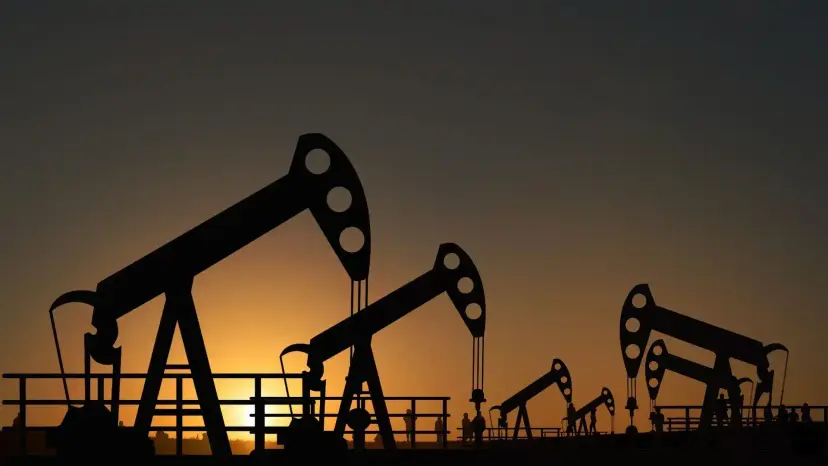 Silhouettes of oil pump jacks against an orange sunset sky.