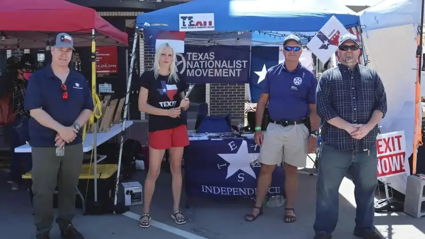 Four Texas Nationalist Movement volunteers stand in front of their booth tent at an outdoor street event.