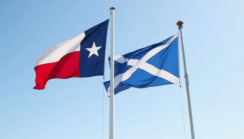 The Texas flag and the Scottish Saltire fly side by side on flagpoles against a clear blue sky.
