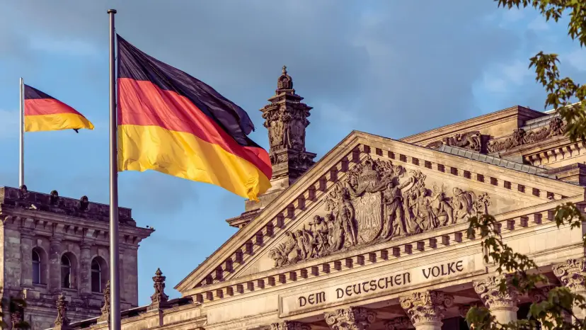 German flags fly over the Reichstag building in Berlin, inscribed 'Dem Deutschen Volke.'