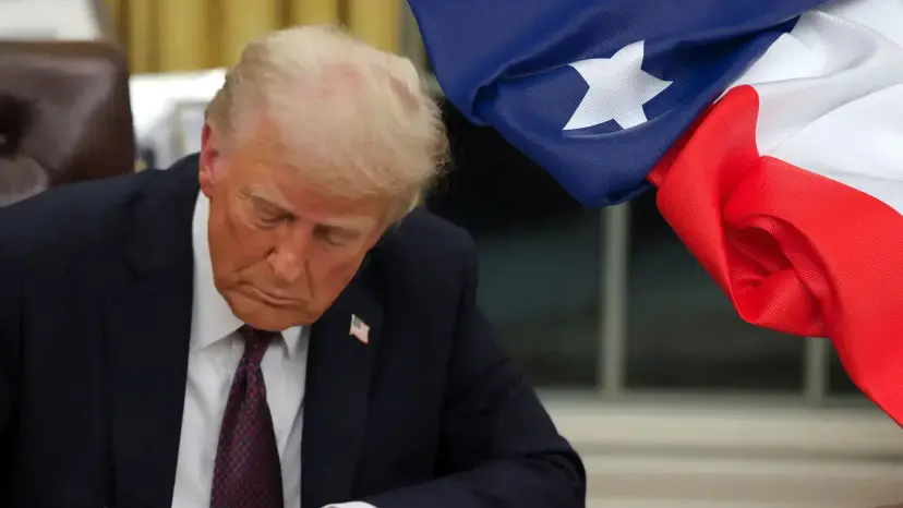 Donald Trump looking down while signing a document, with a Texas flag in the foreground.