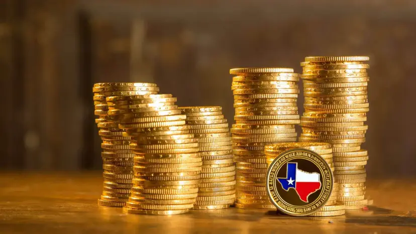 Stacks of gold coins on a wooden table, with a gold coin bearing a Texas flag map in front.