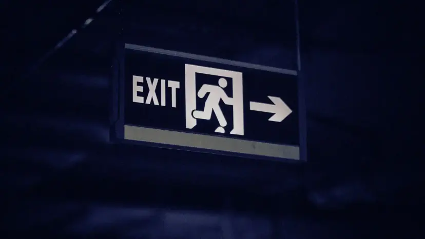 A lit emergency exit sign with a running figure and an arrow pointing right, in dim blue light.