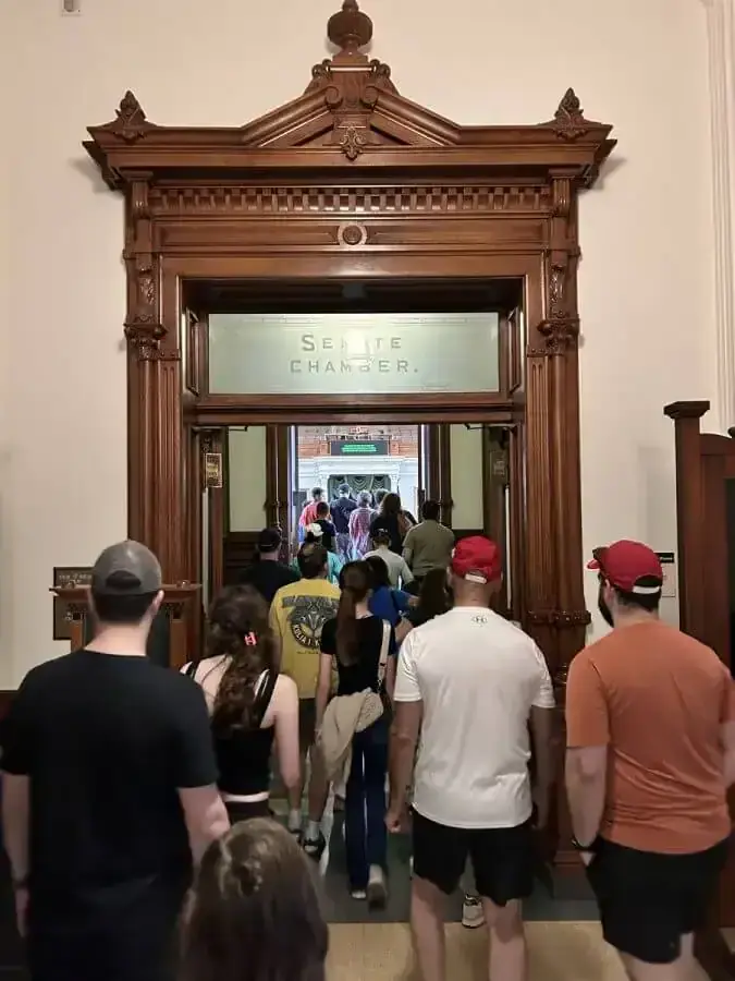 Tour group files through the carved wooden doorway of the Texas Senate Chamber.