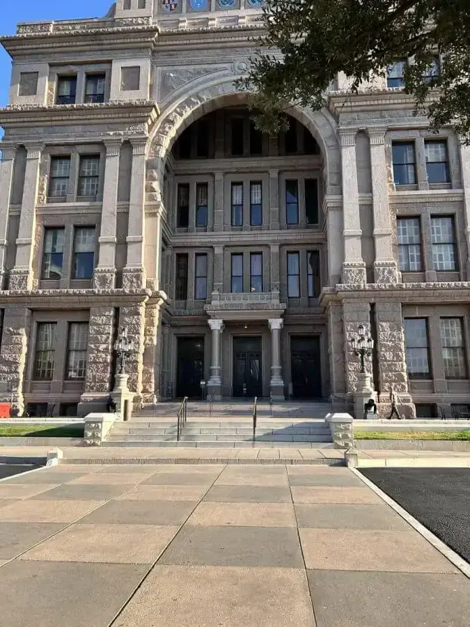 Front entrance of the Texas Capitol, with its granite arch and steps, seen from the plaza.