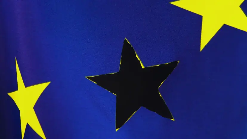 Close-up of the European Union flag with one gold star cut out, leaving a dark star-shaped hole.