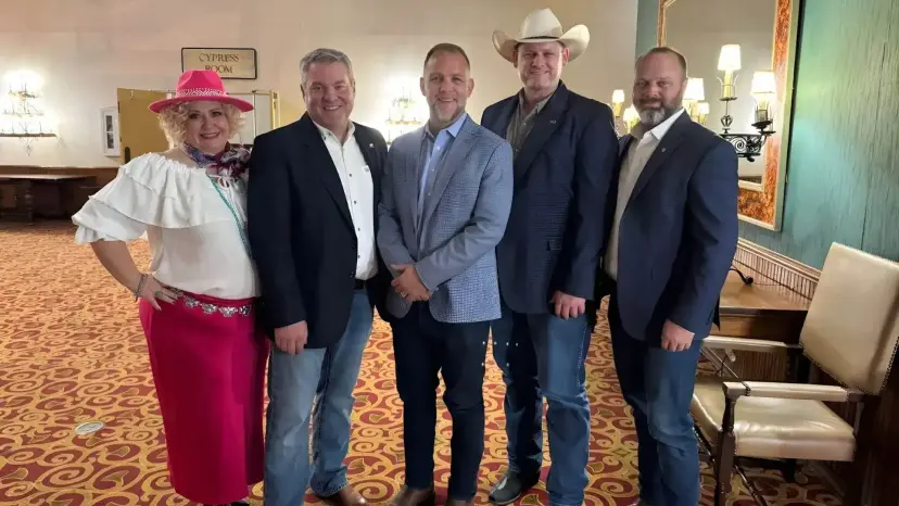 Five people in dress clothes and cowboy hats pose together in a hotel ballroom with patterned carpet.