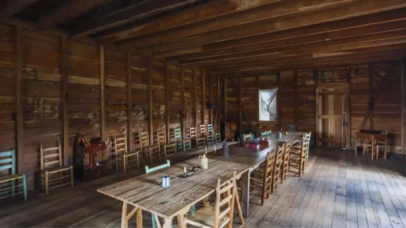 Interior of Independence Hall at Washington-on-the-Brazos, with plank tables and ladder-back chairs in a rough wooden room.