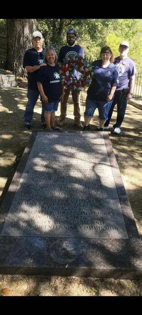 Five TNM members hold a red, white and blue wreath behind Juan Seguin's engraved granite grave marker.