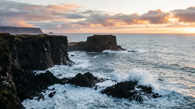 Dramatic Icelandic North Atlantic coastline at golden hour, black basalt sea cliffs and crashing surf under a moody sky, with distant sea stacks on the horizon