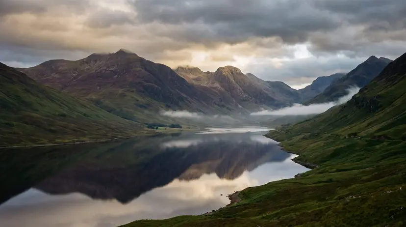 A dramatic Scottish Highlands glen at dusk, a still loch mirroring heather-covered mountains under a moody, cloud-filled sky with golden light breaking through