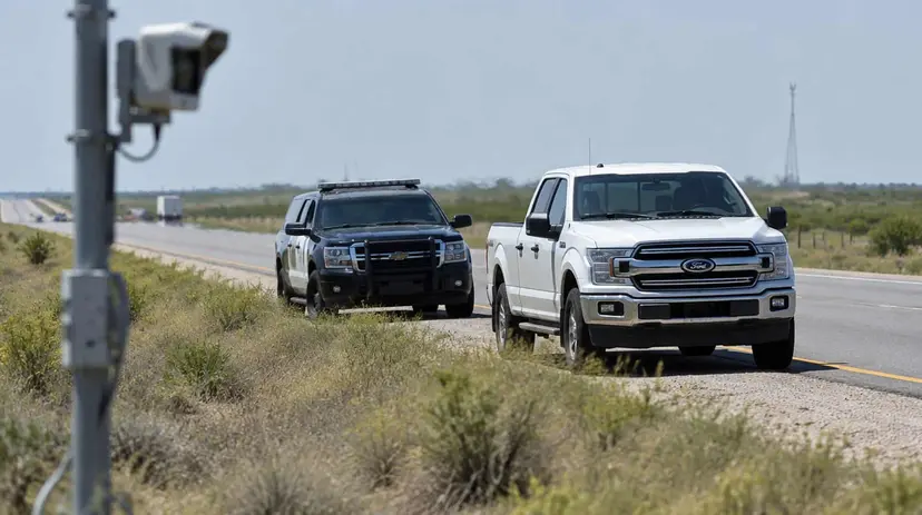 A pickup truck stopped on the shoulder of a South Texas highway with a patrol vehicle behind it and a roadside camera in the foreground.