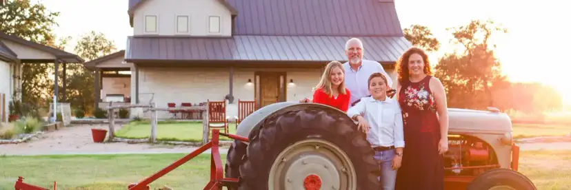 Family of four posing beside a vintage tractor in front of a farmhouse at sunset
