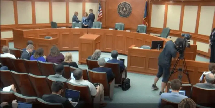 A Texas House committee hearing room with witnesses at the front, a seated audience, and a camera operator filming.