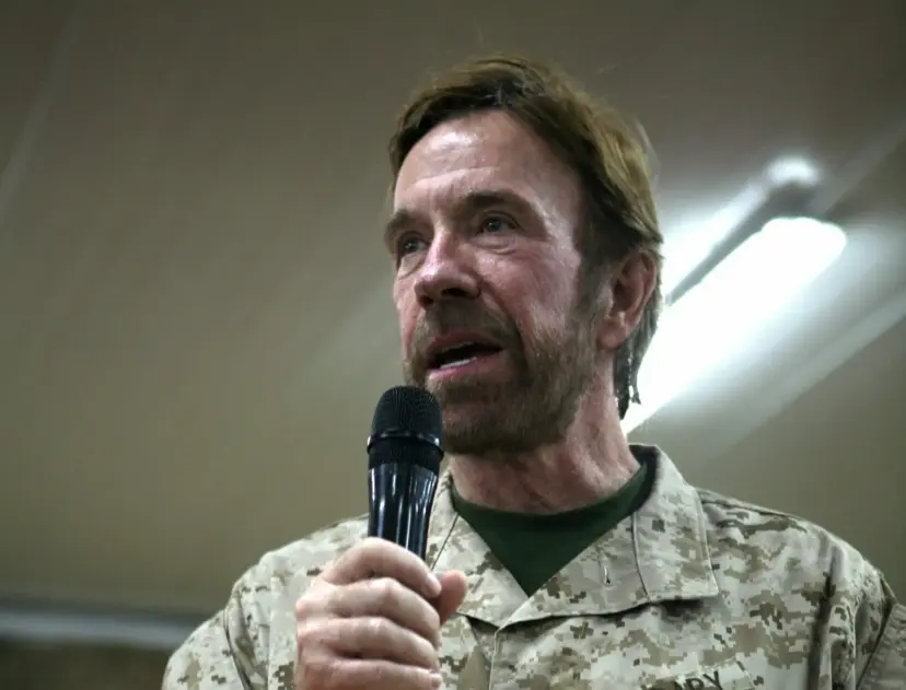 Chuck Norris in a camouflage shirt speaking into a handheld microphone.
