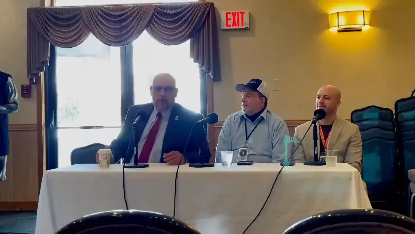 Daniel Miller speaks on a panel with two other men seated at a table with microphones.