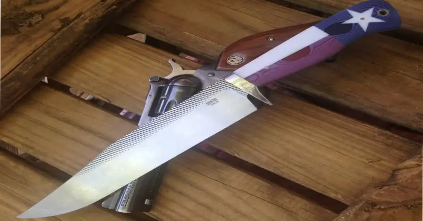 Large knife with a Texas flag handle resting on a revolver atop a wooden surface.